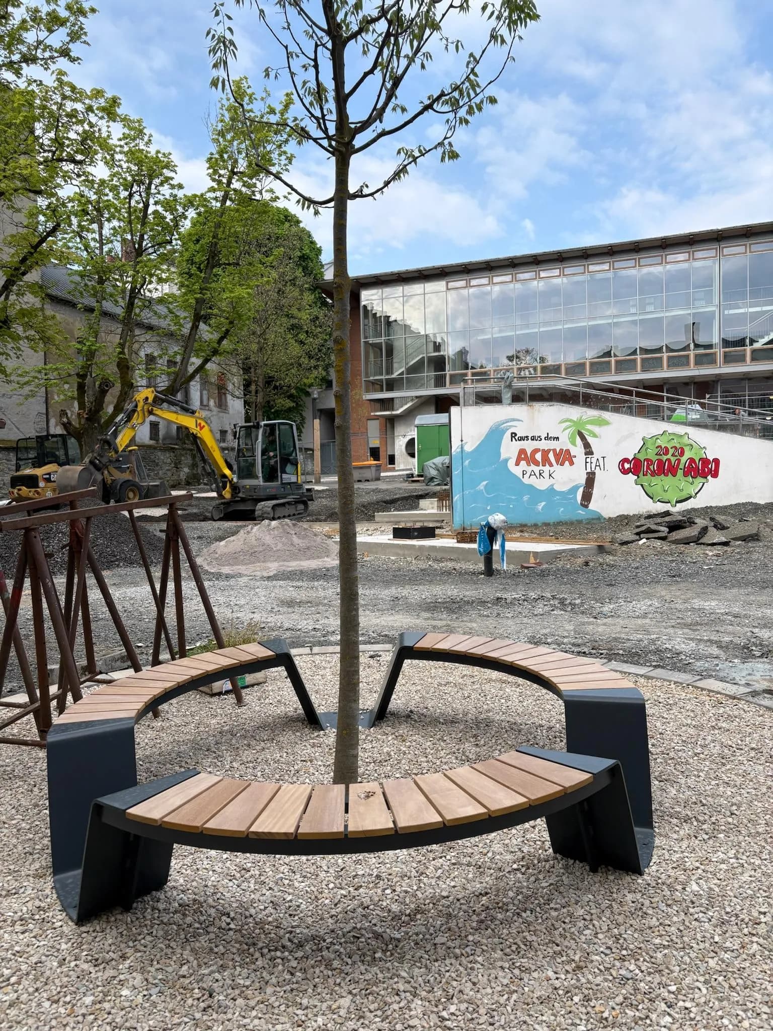 Neue runde Holzbänke um einen frisch gepflanzten Baum auf dem Schulhof